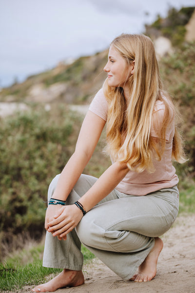 Christian model wearing Made 4 Ministries Child of God azure blue silver cross braided friendship bracelet by Rizen Jewelry. Layered with Joyful Be Magnified multi cord bracelet and Crown of Thorns Beaded bracelets.