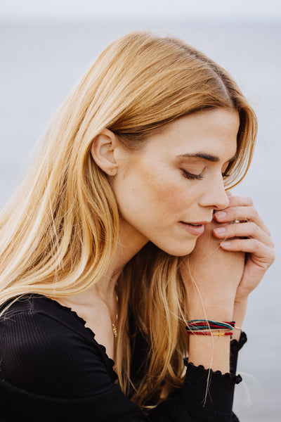 Christian model wearing Made 4 Ministries Child of God garnet red gold cross braided friendship bracelet by Rizen Jewelry. Layered with Faithful Be Magnified braclet and Mini Gold Cross Stud Earrings. 