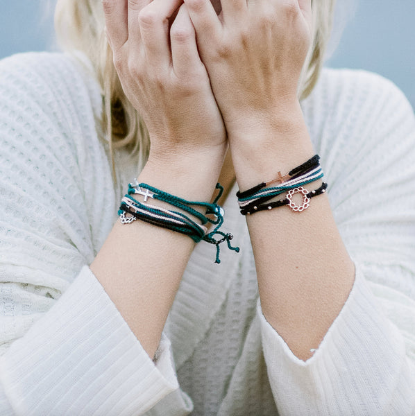 Christian Model wearing Made 4 Ministries Child of God black rose gold cross braided friendship bracelet by Rizen Jewelry. Layered with cross, crown of thorns and joyful Be Magnified bracelets.