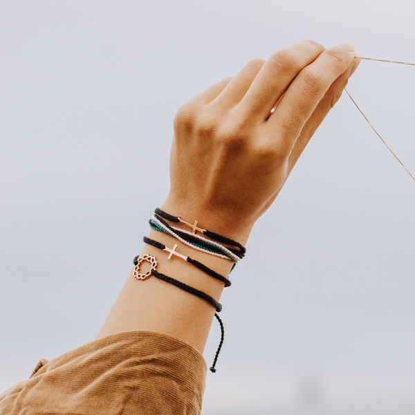 Rizen Jewelry Christian model wearing black Rose Gold Stay Salty Cross Bracelet layered with faith inspired macrame friendship bracelets. 