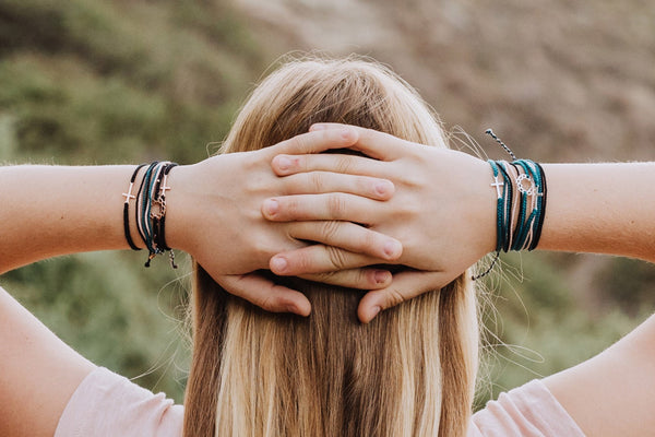 Model wearing christian friendship bracelet with silver crown of thorns pendant on hand braided azure blue cotton cords by Rizen Jewelry. Layered with multiple Made 4 Ministries collection bracelets.