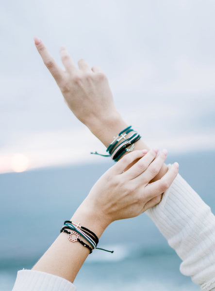 Christian model wearing Rose Gold cross bracelet engraved "STAY SALTY" hand braided black cotton cords by Rizen Jewelry. Layered with multiple Made 4 Ministries cross, crown of thorns, and multicord bracelets. 